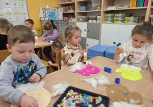 Dzieci wykonują pracę plastyczną „Zimowa rękawica” przy stolikach.