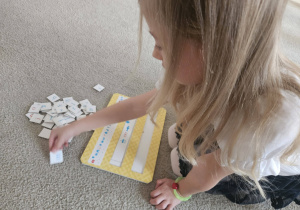 Dziecko siedzi na dywanie i układa literki według kodu na planszy.