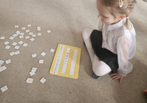 Dziecko siedzi na dywanie obok rozsypanych liter i planszy do kodowania.