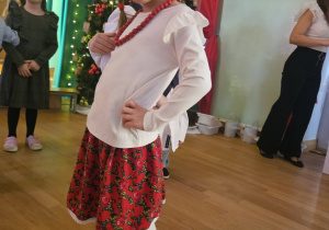 Dziewczynka w stroju ludowym stoi na scenie podczas świątecznego występu.