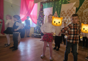 Dzieci wykonują układ taneczny na sali udekorowanej w świątecznym klimacie.