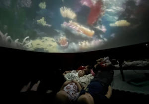 Dzieci leżą na matach i oglądają podwodną projekcję wyświetlaną na suficie balonu.
