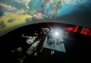 Widok wnętrza kina sferycznego z dziećmi leżącymi podczas seansu.