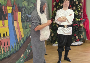 Aktorzy w przebraniach rozmawiają ze sobą na scenie podczas spektaklu teatralnego.