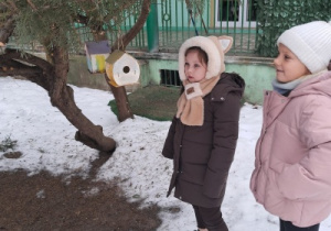 Dwoje dzieci ogląda karmnik dla ptaków zawieszony na drzewie.
