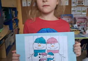 Dziewczynka trzyma pracę z zimowym obrazkiem i liczbami.