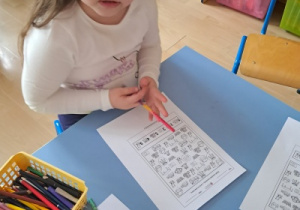 Dziecko przy stoliku rozwiązuje kartę pracy z zadaniami.