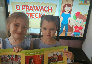 Dwie dziewczynki prezentują planszę edukacyjną dotyczącą praw dziecka.