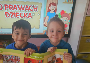 Dwoje dzieci trzyma planszę „Prawa dziecka” i uśmiecha się do zdjęcia.