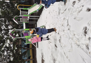 Dzieci bawią się na zaśnieżonym placu zabaw obok zjeżdżalni.