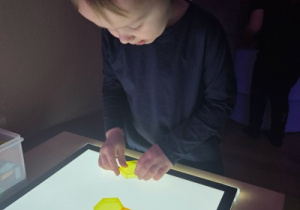 Dziecko układa klocki na świecącym panelu świetlnym, ćwicząc koncentrację i motorykę.