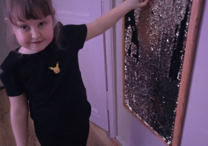 Dziewczynka dotyka sensorycznej tablicy z ruchomymi elementami, badając jej fakturę.