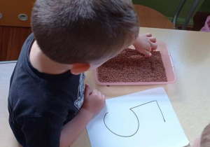 Chłopiec kreśli wzory na tacy z kaszą.