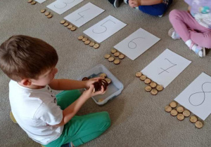 Chłopiec podnosi z tacy kółka z drewna i przelicza je.