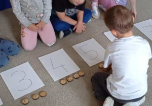 Chłopiec układa odpowiednią ilość drewnianych krążków pod kartkami z zapisanymi cyframi.