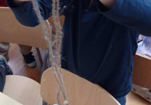 Dziewczynka przywiązuje sznurek do plastikowej butelki i robi supeł do zawieszenia karmnika.