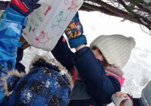 Chłopiec i dziewczynka przechylają plastikowe kubeczki z ziarnami i nasypują ziarna do karmnika.