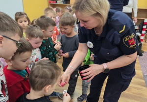 Funkcjonariuszka Straży Miejskiej wręcza dzieciom naklejki.