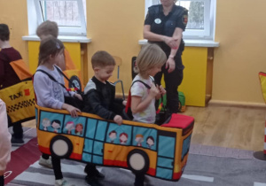 Dzieci w makiecie autobusu uczestniczą w zabawie edukacyjnej na macie przedstawiającej drogę.