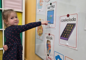 Dziewczynka stoi przy tablicy. Wskazuje obrazek związany z Walentynkami.