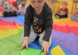 Chłopiec siedzi na chuście. Układa puzzle w kształcie serca.