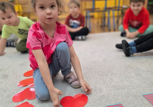 Dziewczynka kładzie papierowe serce przy kartoniku z cyfrą. Ćwiczy liczenie.