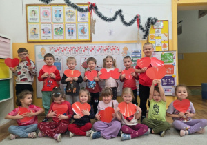 Grupa dzieci trzyma duże czerwone serca. Dzieci stoją i siedzą do wspólnego zdjęcia.