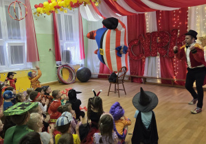 Dzieci oglądają występ cyrkowy w kolorowo udekorowanej sali.