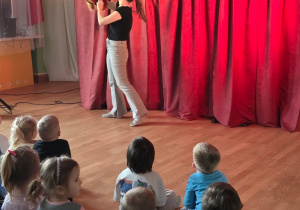 Aktorka trzyma siatkę, w której znajduje się kukiełka lisa, na tle czerwonej sceny.