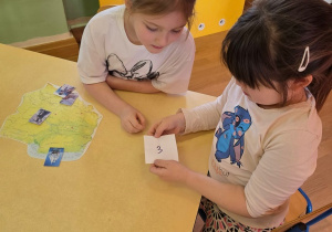 Dwie dziewczynki przy stoliku wylosowały kartonik z numerem; zaraz odpowiedzą na pytanie związane z Polską,