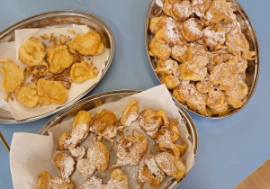 Gotowe pączki posypane cukrem pudrem ułożone na metalowych tacach.