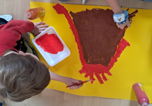 Dzieci malują duży plakat przedstawiający wulkan podczas zajęć o dinozaurach.