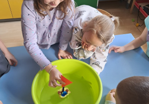 Dzieci obserwują małą łódkę unoszącą się na wodzie w misce podczas doświadczenia.