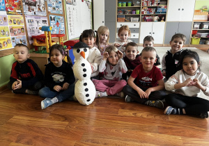 Dzieci w sali przedszkolnej siedzą obok wykonanego przez siebie bałwana.