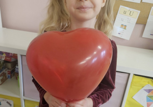 Dziewczynka trzyma czerwony balon w kształcie serca podczas walentynkowych zajęć w sali.
