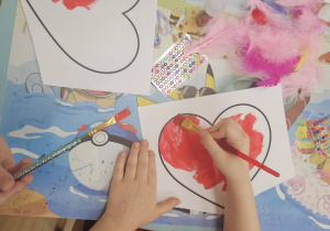 Dzieci malują czerwone serca podczas pracy plastycznej.