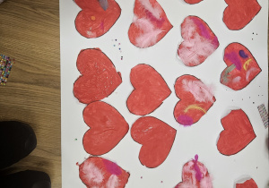 Wspólna praca plastyczna dzieci - czerwone serca ozdobione piórkami i cekinami.