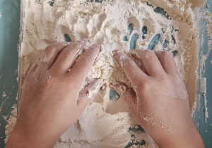 Dziecko bawi się mąką podczas zajęć sensorycznych.