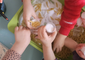 Dzieci przesypują makaron i sól podczas zajęć sensorycznych.