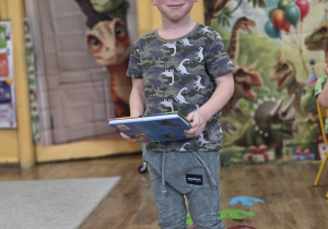 Chłopiec stoi na śladach dinozaura podczas zabawy ruchowej.