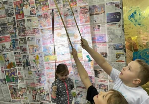 Dwójka dzieci maluje długimi pędzlami na gazetach