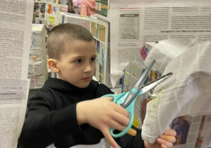 Chłopiec tnie gazety nożyczkami