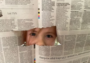Dziewczynka patrzy przez dziurę w gazecie