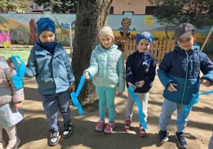 Dzieci trzymają niebieskie wstążki i kibicują.