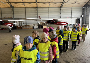 Dzieci zwiedzają hangar i poznają pracę lotniska.