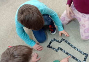 Dzieci układają domino na dywanie.