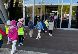 Zdjęcie przedstawiające dzieci przechodzące przez pasy wchodzące na terminal lotniska.