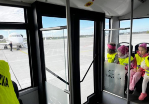Zdjęcie przedstawiające dzieci jadące autobusem po płycie lotniska.