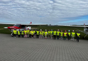 Zdjęcie grupowe dzieci na tle samolotów płyty lotniska.