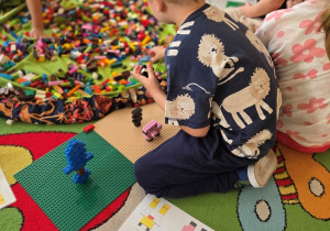 Chłopiec siedzi na dywanie i buduje konstrukcję z klocków LEGO.